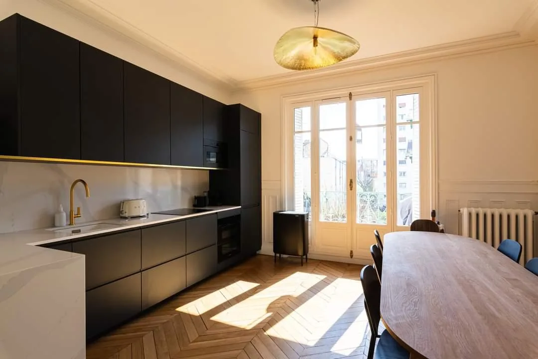 Cuisine noire mate à liseré laiton sous corniche haussmannienne, parquet point de Hongrie