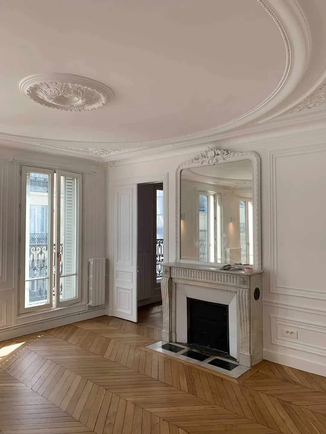 Réception haussmannienne restaurée — rosace, corniches sculptées et cheminée en marbre blanc, parquet point de Hongrie